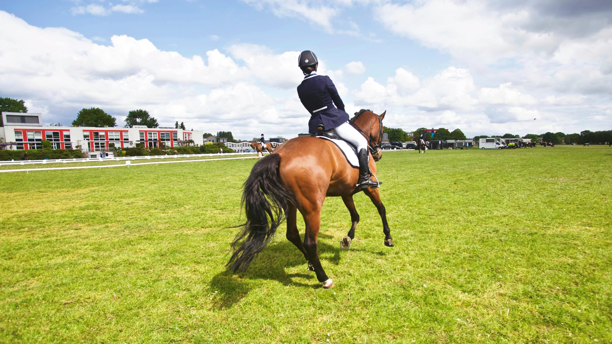 A horse rider participating in a dressage event outdoors under a bright sky.